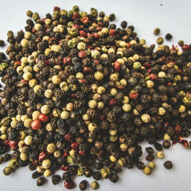 A close-up view of mixed peppercorns showcasing vivid colors on a white background.