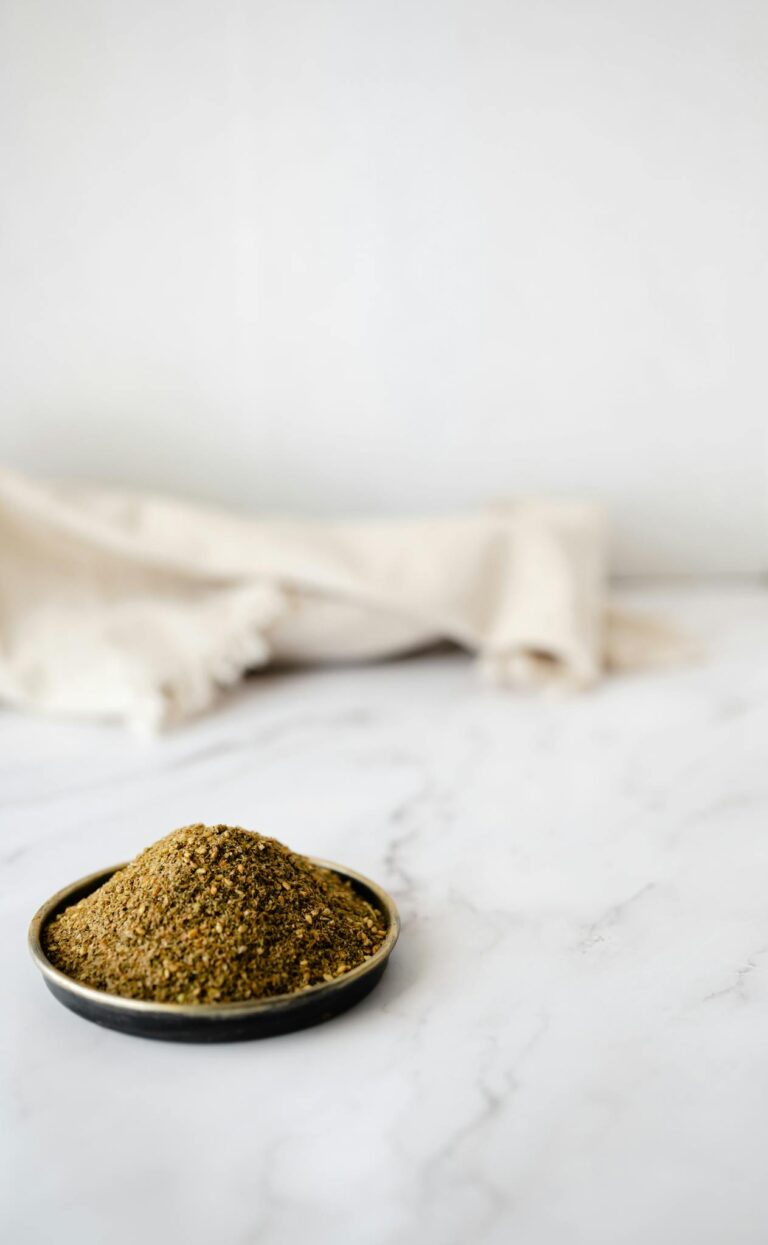 Close-up of a green spice mix in a black bowl with a neutral background, perfect for culinary themes.