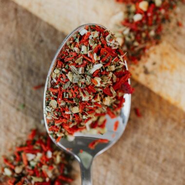 Close-up of mixed herbs and spices on a spoon over wooden surface.