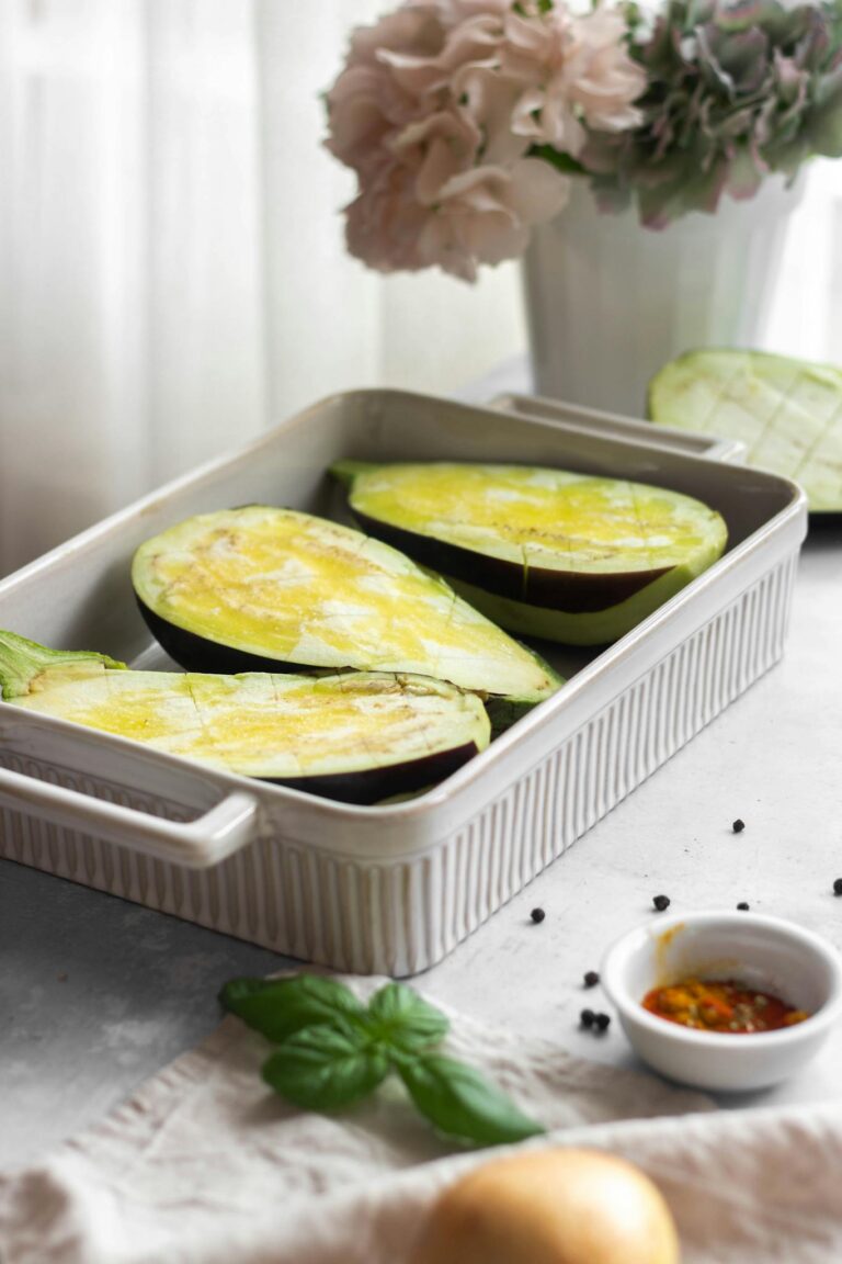 Vertical shot of eggplant halves with spices in a baking dish on a light background.