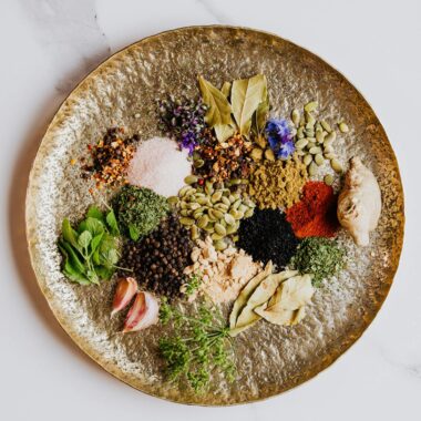 Vibrant spices and herbs artfully arranged on a textured round plate, showcasing a diverse culinary palette.